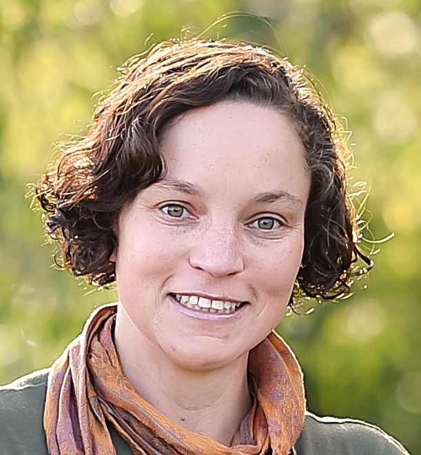 Sarita has light skin, short wavy brown hair, and green eyes. She is smiling with head tilted slightly.